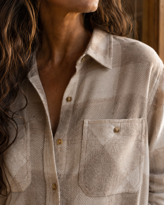 Close-up of a woman wearing a light beige plaid button-up shirt with a chest pocket and gold-tone buttons.