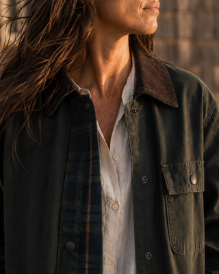 A close-up lifestyle shot of a person wearing a dark olive green overshirt with a brown corduroy collar over a white button-down shirt and a navy plaid shirt.